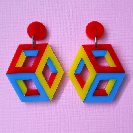 Colourful red, blue and yellow statement geometric cube earrings on a pink background