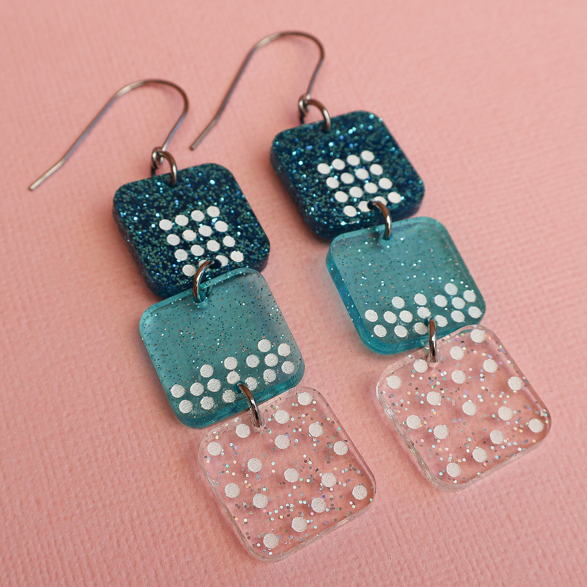States of matter earrings closeup showing  components with solid, liquid and gas particles, in teal colours. 