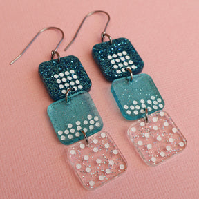 States of matter earrings closeup showing  components with solid, liquid and gas particles, in teal colours. 