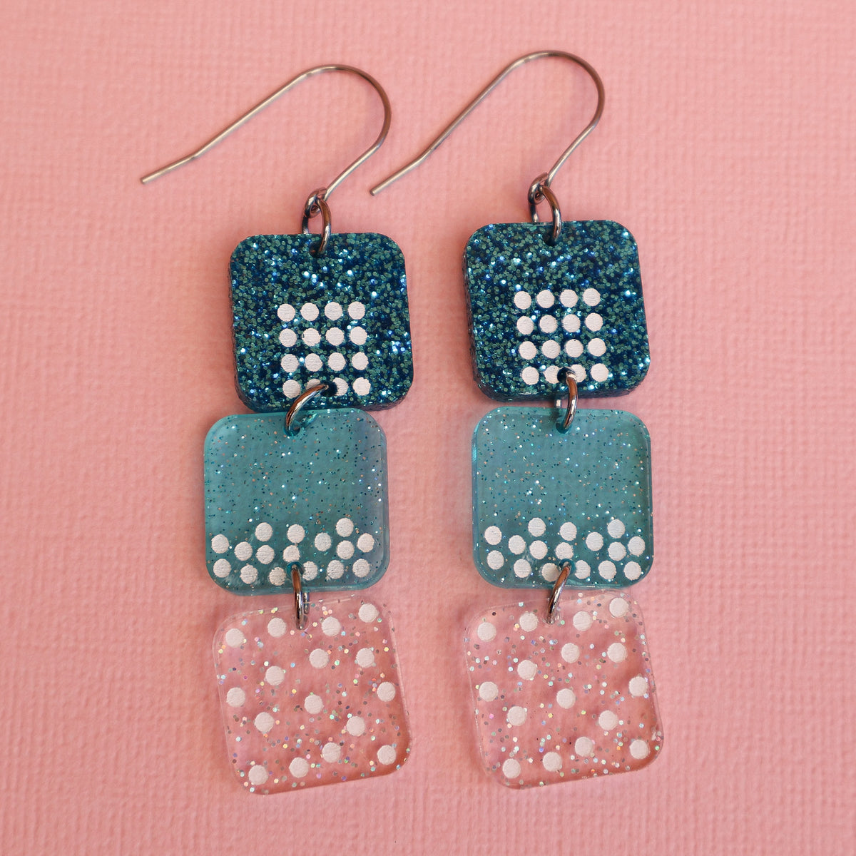 States of matter earrings closeup showing  components with solid, liquid and gas particles, in teal colours. 