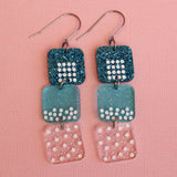 States of matter earrings closeup showing  components with solid, liquid and gas particles, in teal colours. 