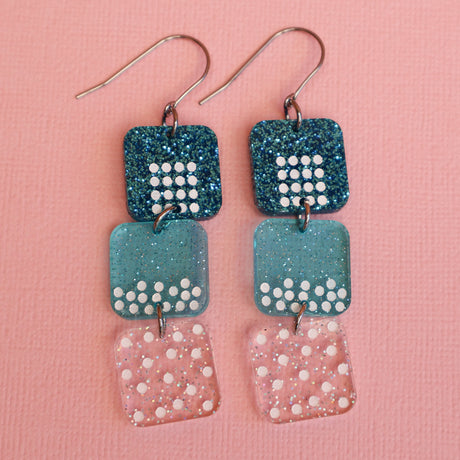 States of matter earrings closeup showing  components with solid, liquid and gas particles, in teal colours. 