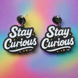 Pair of 'Stay Curious' black glitter acrylic earrings with white text and yellow stars