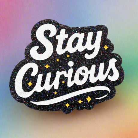 Decorative black glittery brooch with 'Stay Curious' text  and yellow stars