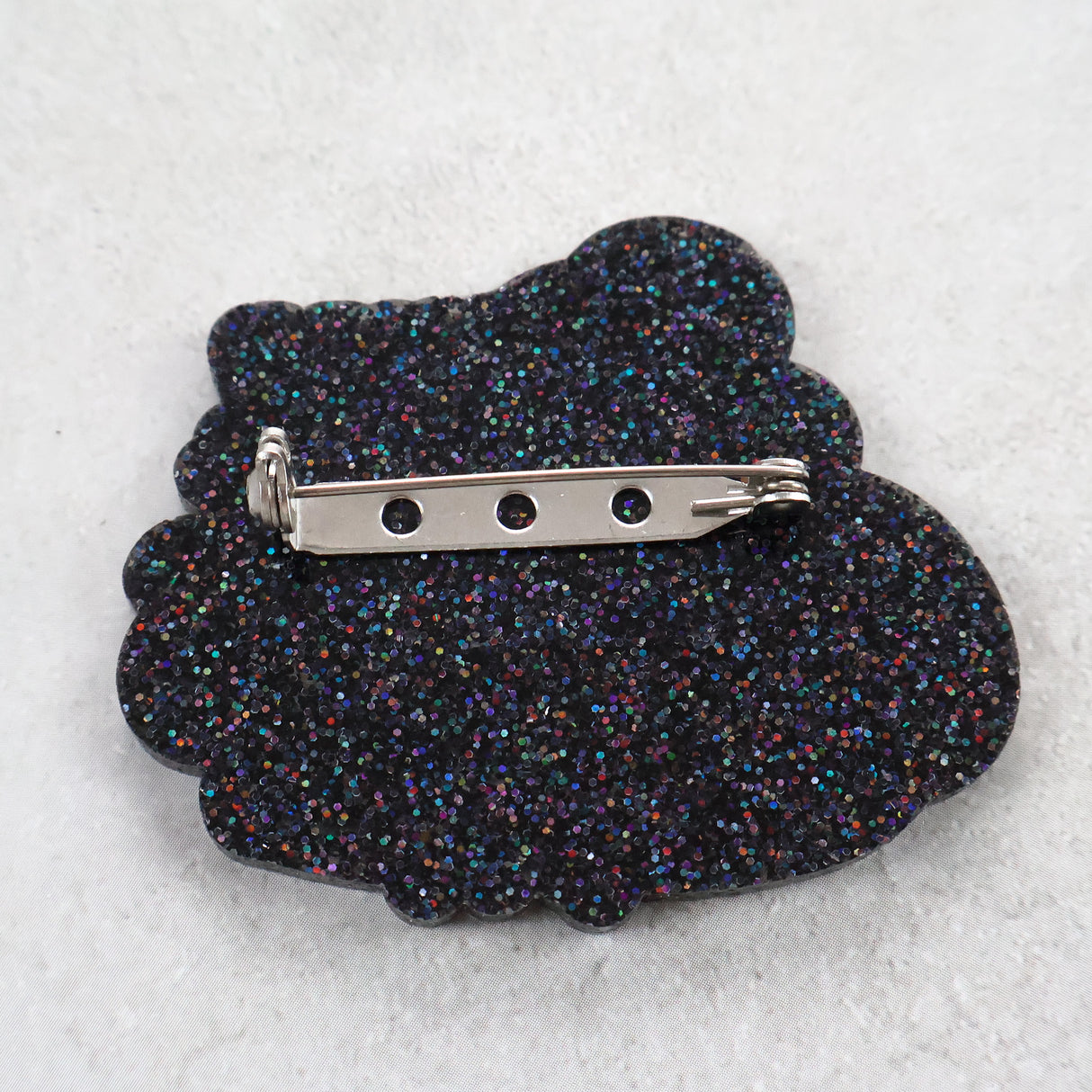 Black glittery brooch back view with a stainless steel brooch pin and rolling clasp. 