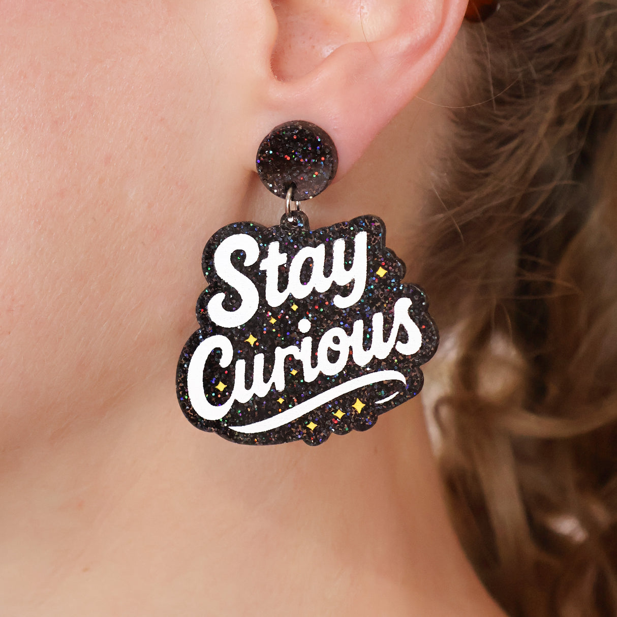 Acrylic dangle earring with 'Stay Curious' text worn by a person