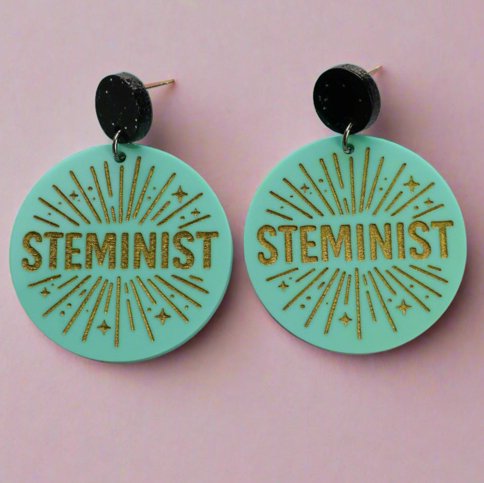 Teal earrings with 'STEMINIST' text on a light pink background
