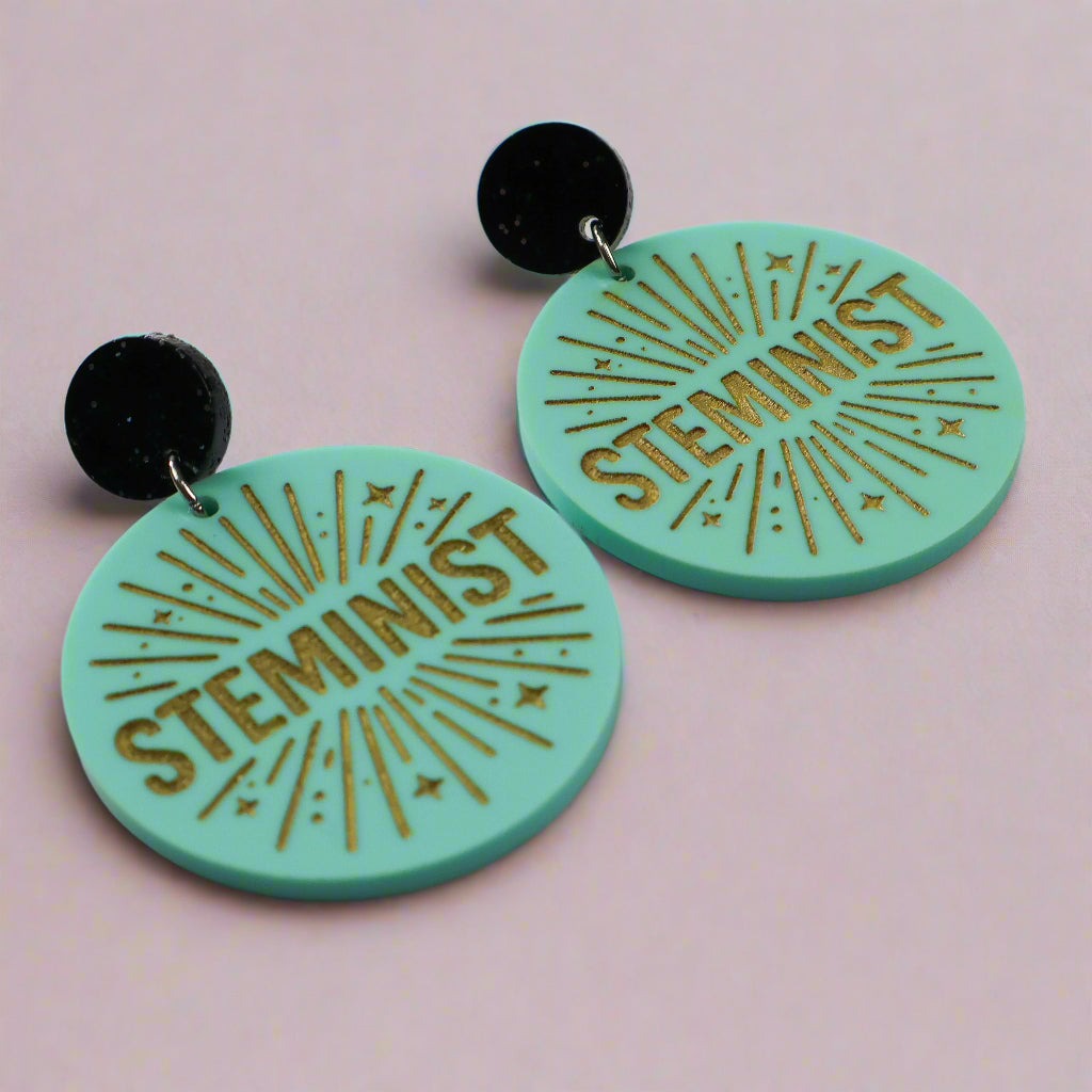 Teal earrings with 'Steminist' text on a light pink background