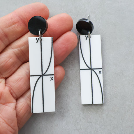 Pair of black and white dangle acrylic earrings with tan graph design held by a hand