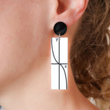 Rectangular acrylic dangles with tan graph printed in black against a white background, and black earring topper. Being modelled. 