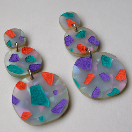 Angled view of Terrazzo dangle acrylic earrings in orange, purple and teal tones. Dangles are 3 components and statements sized. 