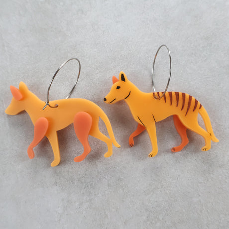 Two orange thylacine or tasmanian tiger shaped earrings with round stainless steel hoops. One earring is flipped over to show the back view. 