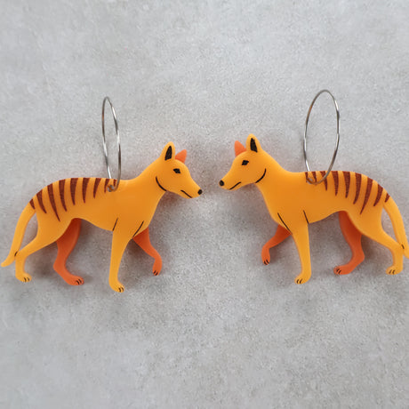 Two orange thylacine or tasmanian tiger shaped earrings with round stainless steel hoops.