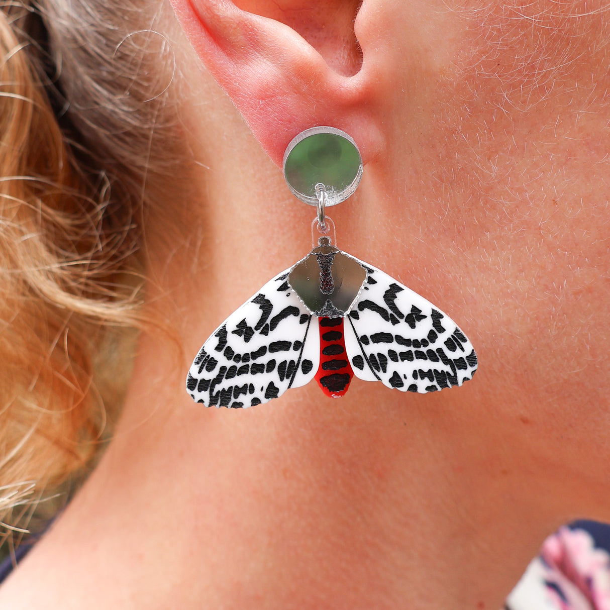 Acrylic tiger moth earrings being modelled. Earrings are black white and red, with silver mirror components.