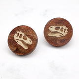 Small round studs in swirly brown acrylic, with T-rex skulls engraved in the center. Design is mirrored on each side