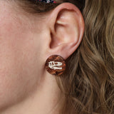 Small studs in swirly brown acrylic, with T-rex skulls engraved in the center. Studs are being modelled. 