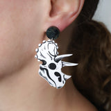 Close-up of a person wearing a black and white triceratops skull dangle acrylic earring.
