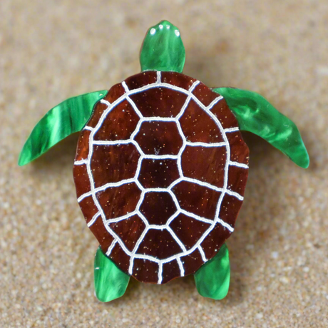 Acrylic turtle brooch with brown shell and green limbs on a sandy background
