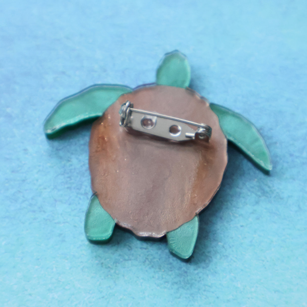 The back view of a turtle-shaped brooch with a metallic clasp on a blue background