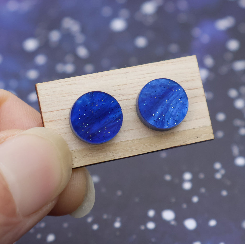 A pair of small blue acrylic studs on a wooden backing card.