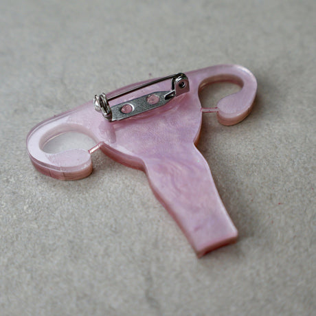 The back view of a laser cut acrylic uterus brooch, showing the stainless steel brooch pin with rolling clasp. 