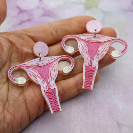 Pink acrylic uterus dangle earrings being held in a hand.