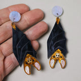 A pair of acrylic vampire bat earrings being held in a hand. Bats hang from light blue/pink earring toppers. 