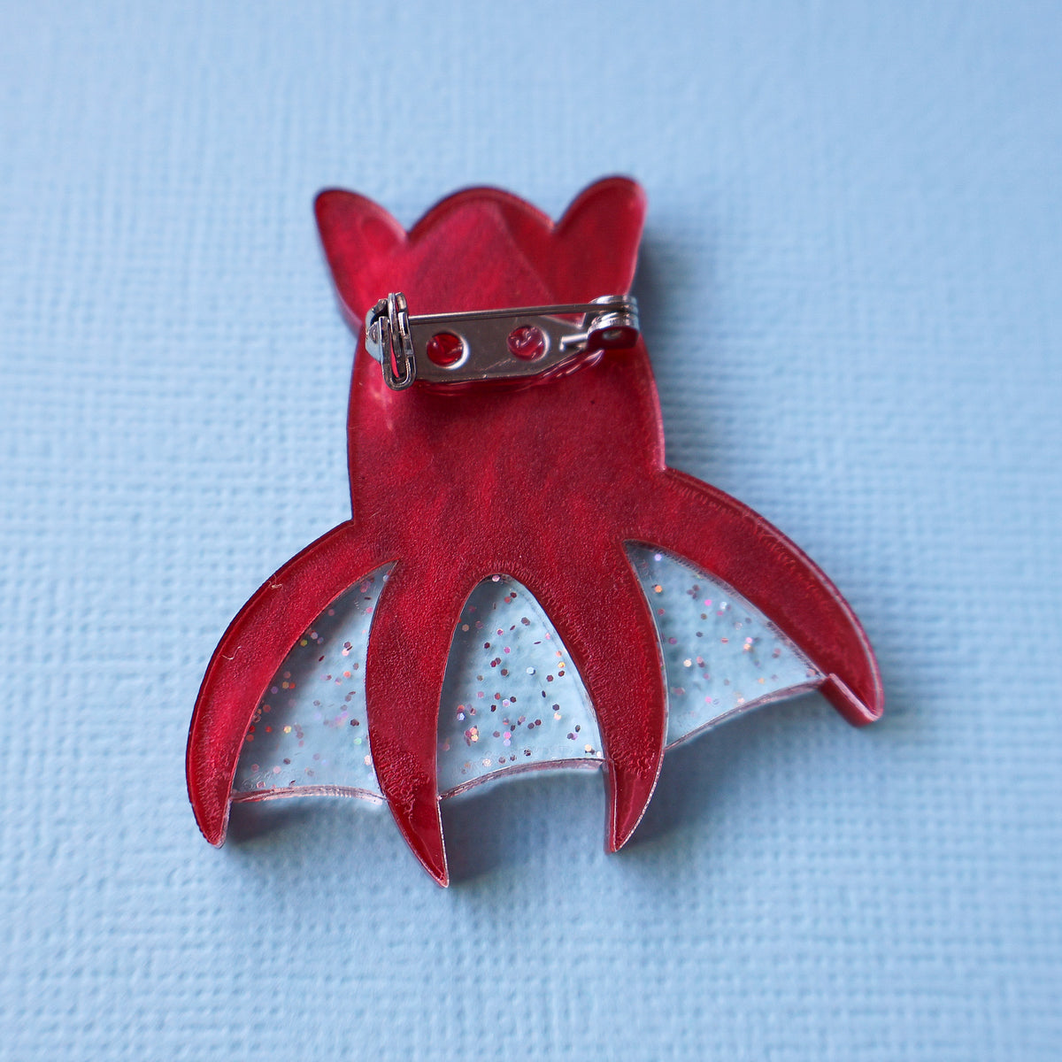 The back view of a red vampire squid brooch showing the stainless steel brooch pin with locking clasp