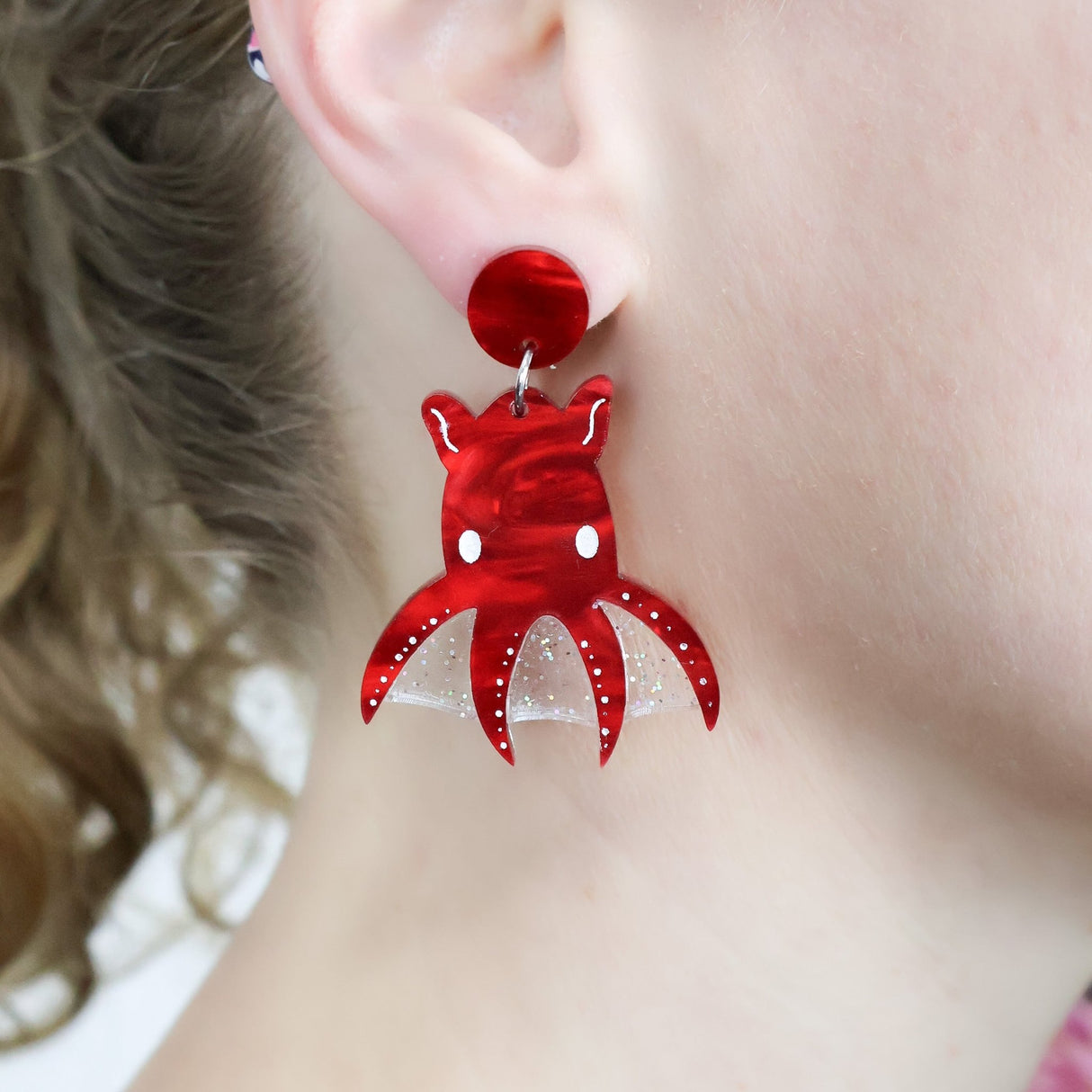 Laser cut acrylic red vampire squid earrings, being modelled.