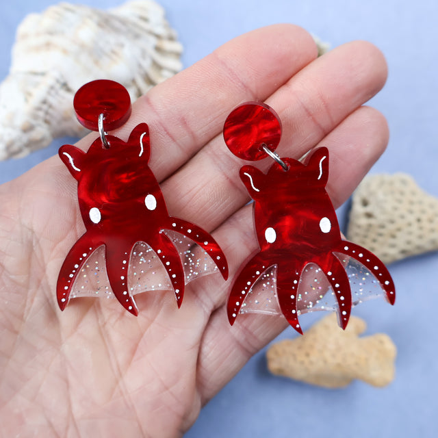 Laser cut acrylic vampire squid earrings, being held in hand.