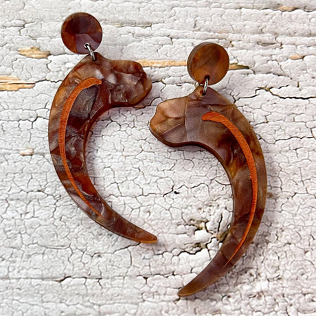 Velociraptor claw earrings, laser cut from textured brown acrylic, and hanging from brown acrylic earring toppers. 