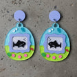 closeup view of a pair of colourful earrings shaped like a virtual pet gaame, displaying sharks. 