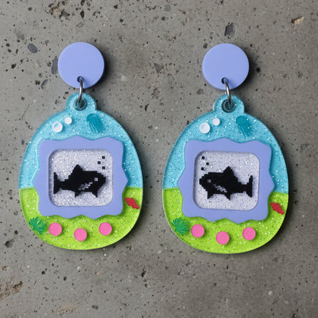 closeup view of a pair of colourful earrings shaped like a virtual pet gaame, displaying sharks. 