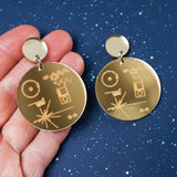 Gold mirror acrylic dangle earrings with engraved design of the voyager golden record held by a hand.