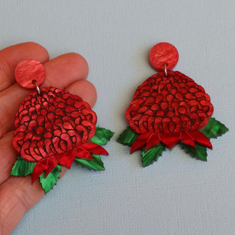 Acrylic waratah earrings being held in a hand