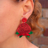 A close-up of a person's ear wearing a waratah dangle earring.
