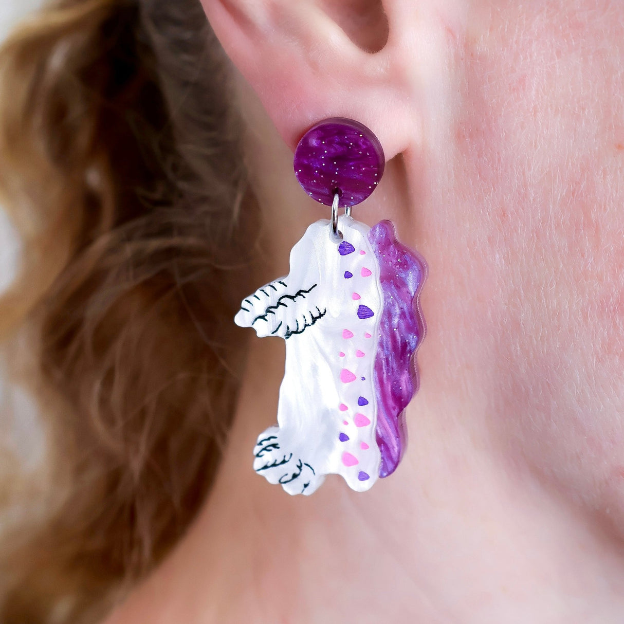 Close-up of a person wearing a sea slug shaped earring with a purple top.