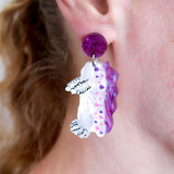 Close-up of a person wearing a sea slug shaped earring with a purple top.