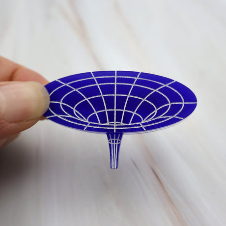 Closeup of dark blue acrylic wormhole brooch, with white handpainted detailing, depicting the warping of spacetime.