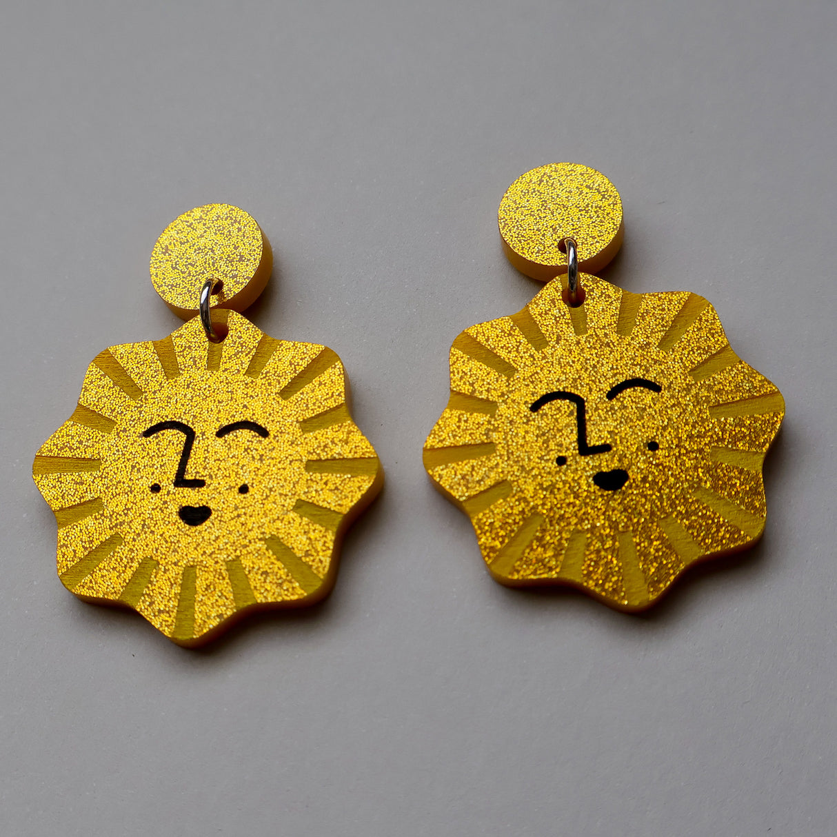 Gold glitter sun-shaped earrings with faces on a gray background