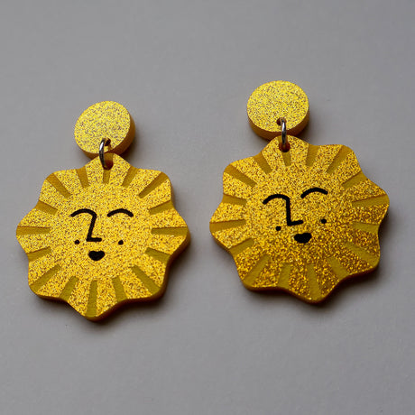Gold glitter sun-shaped earrings with faces on a gray background