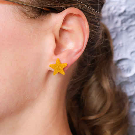Close-up of an ear wearing a gold star-shaped earring with a moonscape backdrop