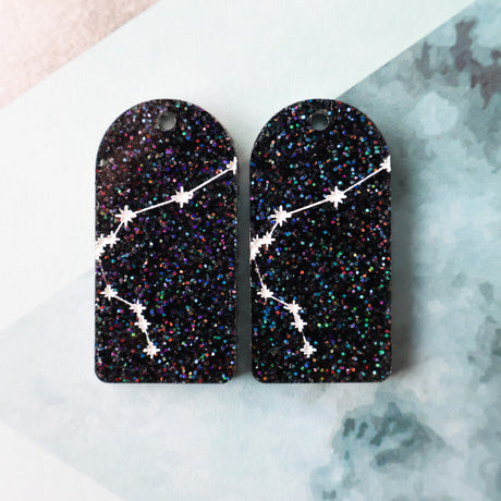 Pair of arch acrylic earrings with aquarius star constellation design in white again black glitter acrylic.