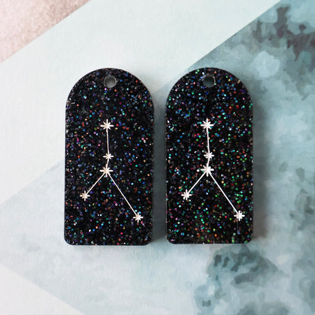 Pair of arch acrylic earrings with aries star constellation design in white again black glitter acrylic.
