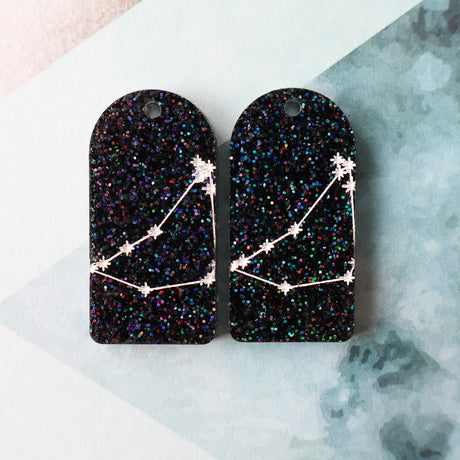 Pair of arch acrylic earrings with capricorn star constellation design in white again black glitter acrylic.