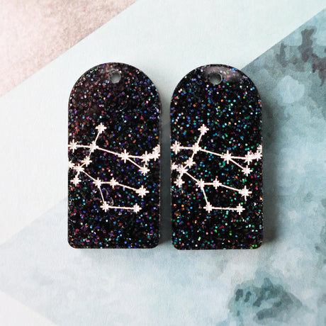 Pair of arch acrylic earrings with gemini star constellation design in white again black glitter acrylic.