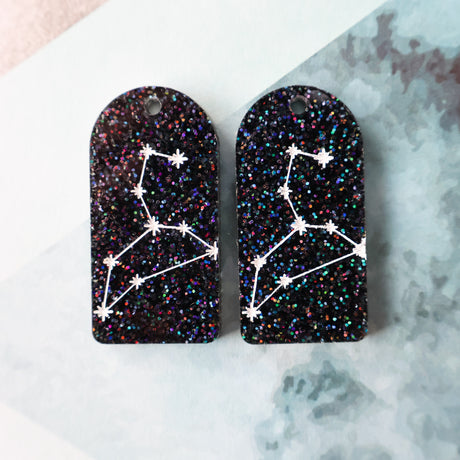 Pair of arch acrylic earrings with leo star constellation design in white again black glitter acrylic.