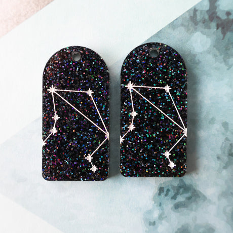 Pair of arch acrylic earrings with libra star constellation design in white again black glitter acrylic.