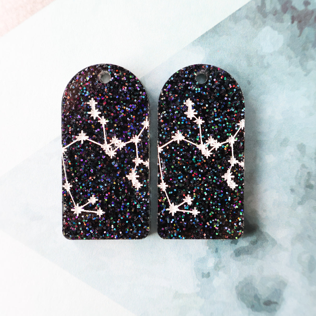 Pair of arch acrylic earrings with saggitarius star constellation design in white again black glitter acrylic.