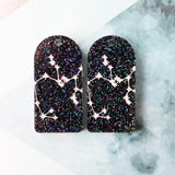 Pair of arch acrylic earrings with saggitarius star constellation design in white again black glitter acrylic.